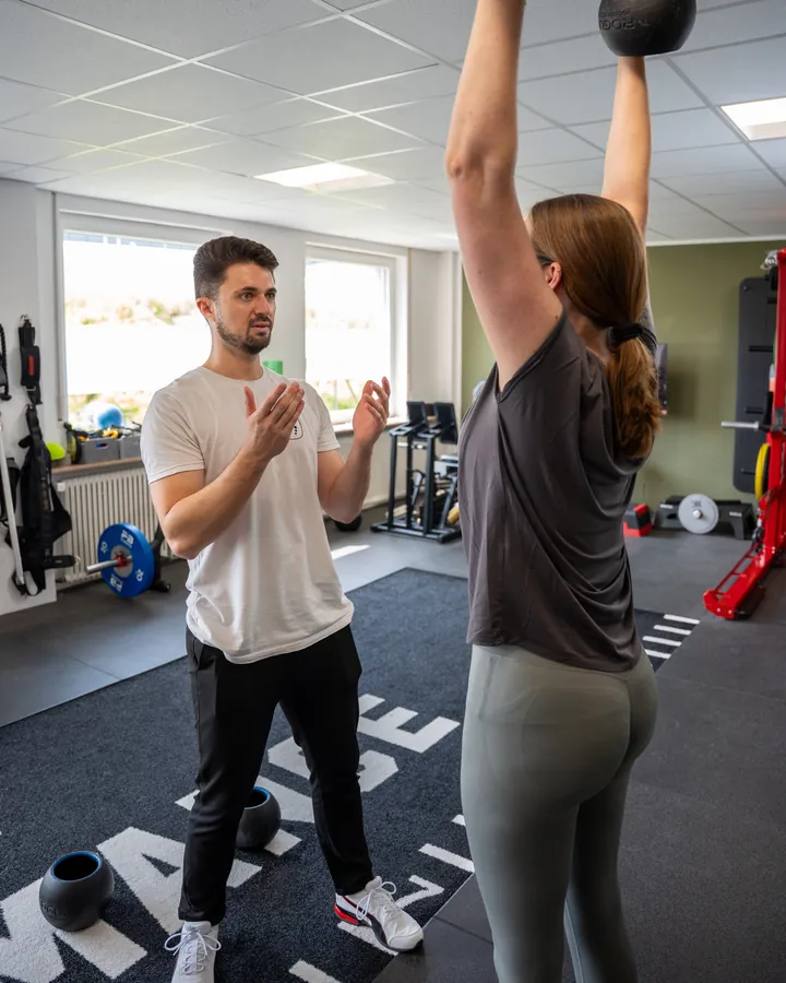 Sportwissenschaftler begleitet eine Patientin beim Training mit dem Medizinball